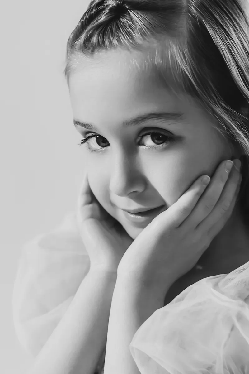 Portrait en noir et blanc d’une jeune fille posant le visage entre ses mains lors d’une séance photo en studio.