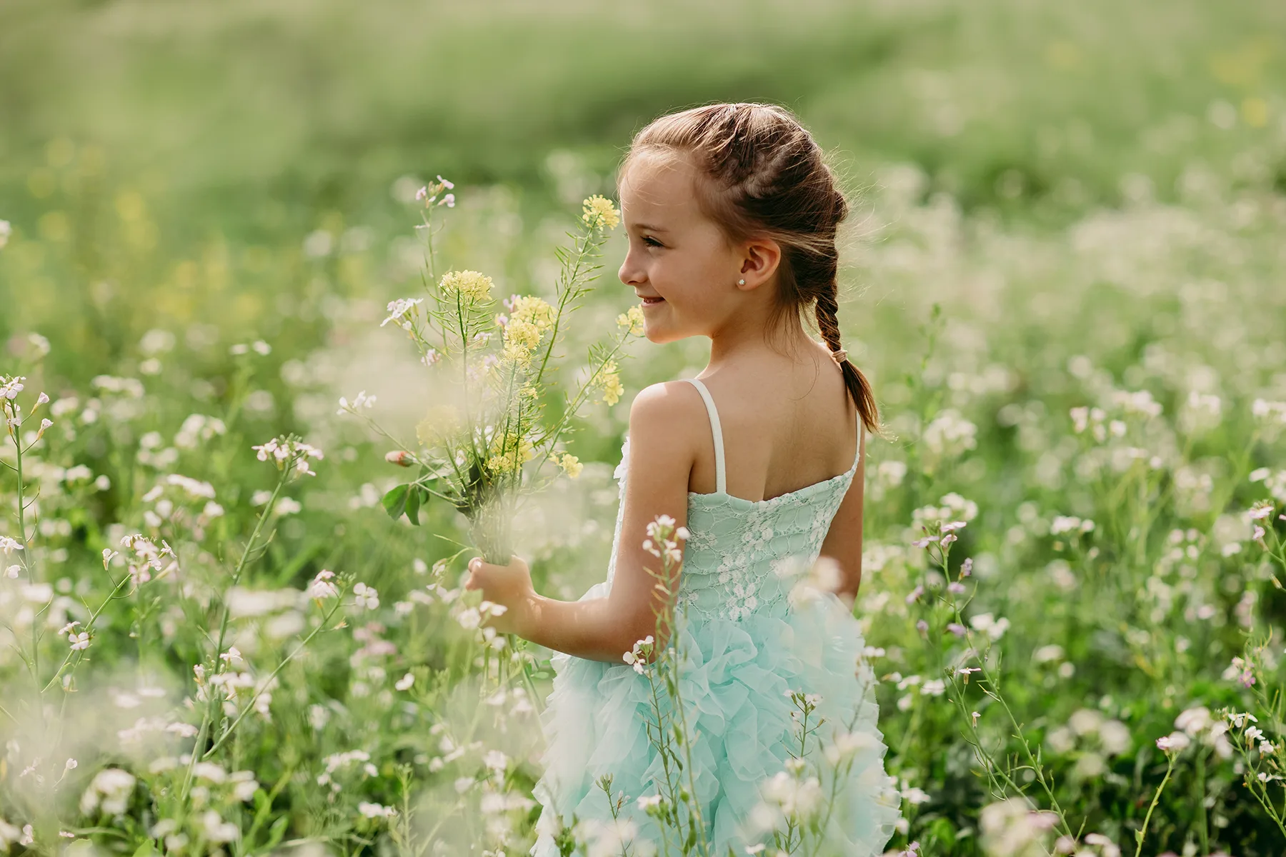 Petite fille en robe bleue cueillant des fleurs sauvages lors d’une séance photo enfant en Provence.