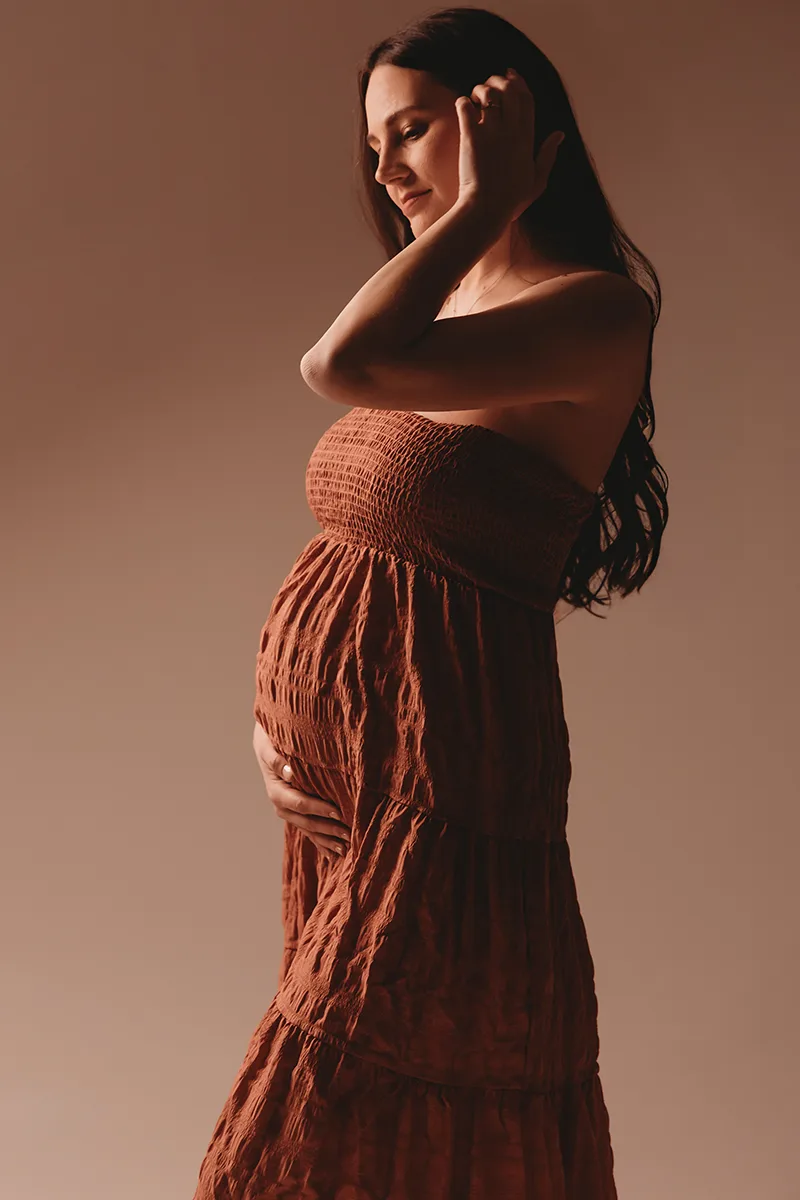 Future maman en robe terracotta photographiée en lumière artistique lors d’une séance grossesse en studio en Provence.