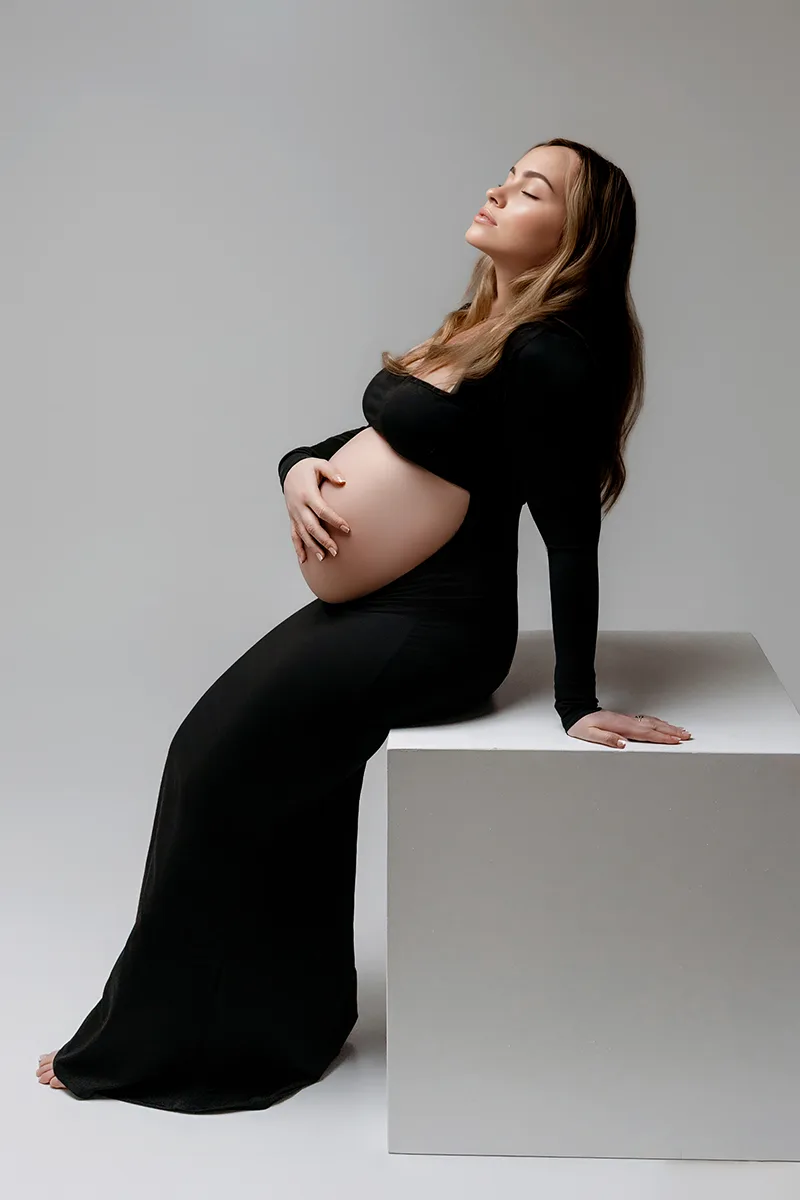 Femme enceinte vêtue de noir posant assise lors d’une séance photo grossesse en studio.