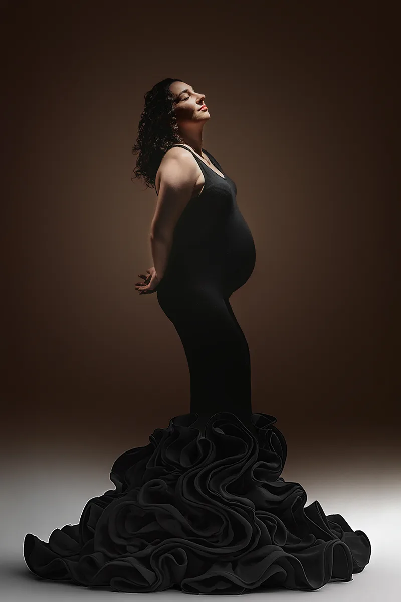 Future maman en longue robe noire photographiée en lumière artistique lors d’une séance grossesse au studio en Provence.