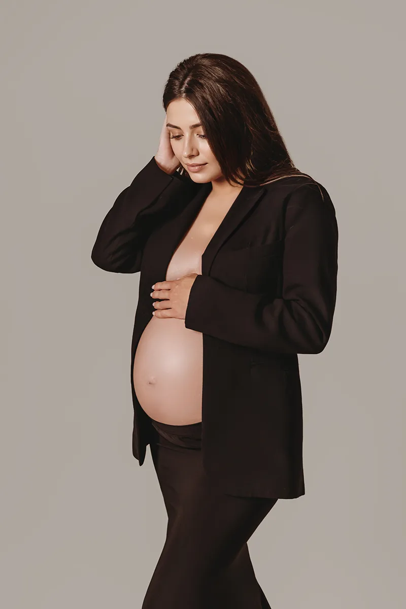 Femme enceinte en jupe et veste noirs posant lors d’une séance photo grossesse moderne en studio.
