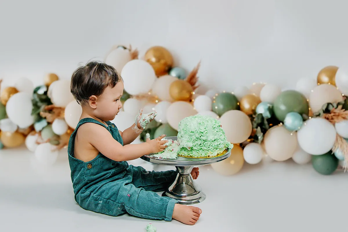 Bébé découvrant son gâteau d’anniversaire vert lors d’une séance photo « smash the cake » en studio.