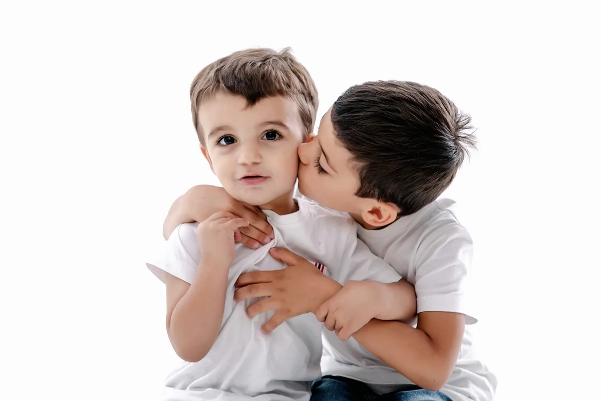 Deux frères partageant un moment complice lors d’une séance photo enfants sur fond blanc au studio.