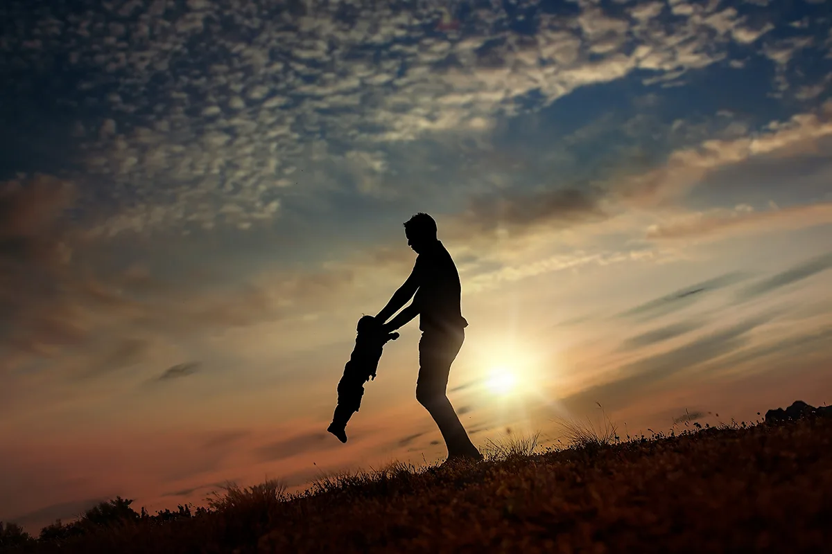 Papa jouant avec son enfant en silhouette devant un coucher de soleil en Provence.