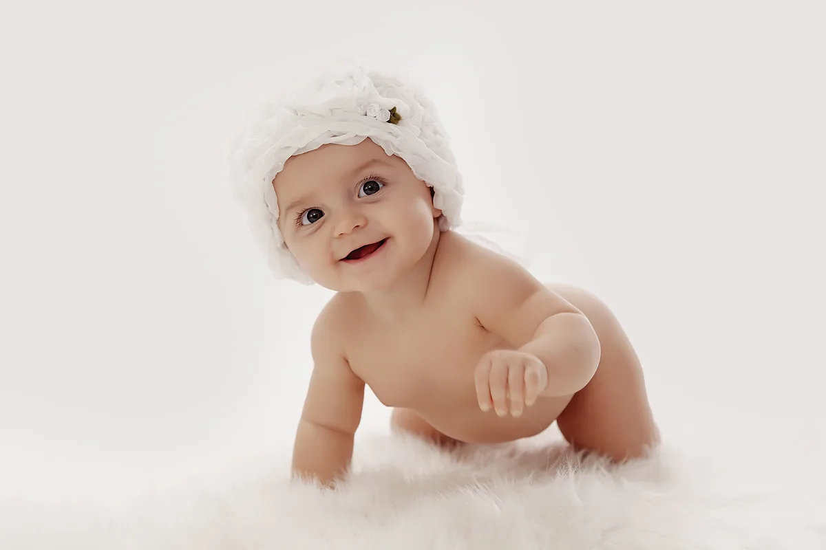 Bébé souriant à quatre pattes, coiffé d’un bonnet blanc, lors d’une séance photo en studio.