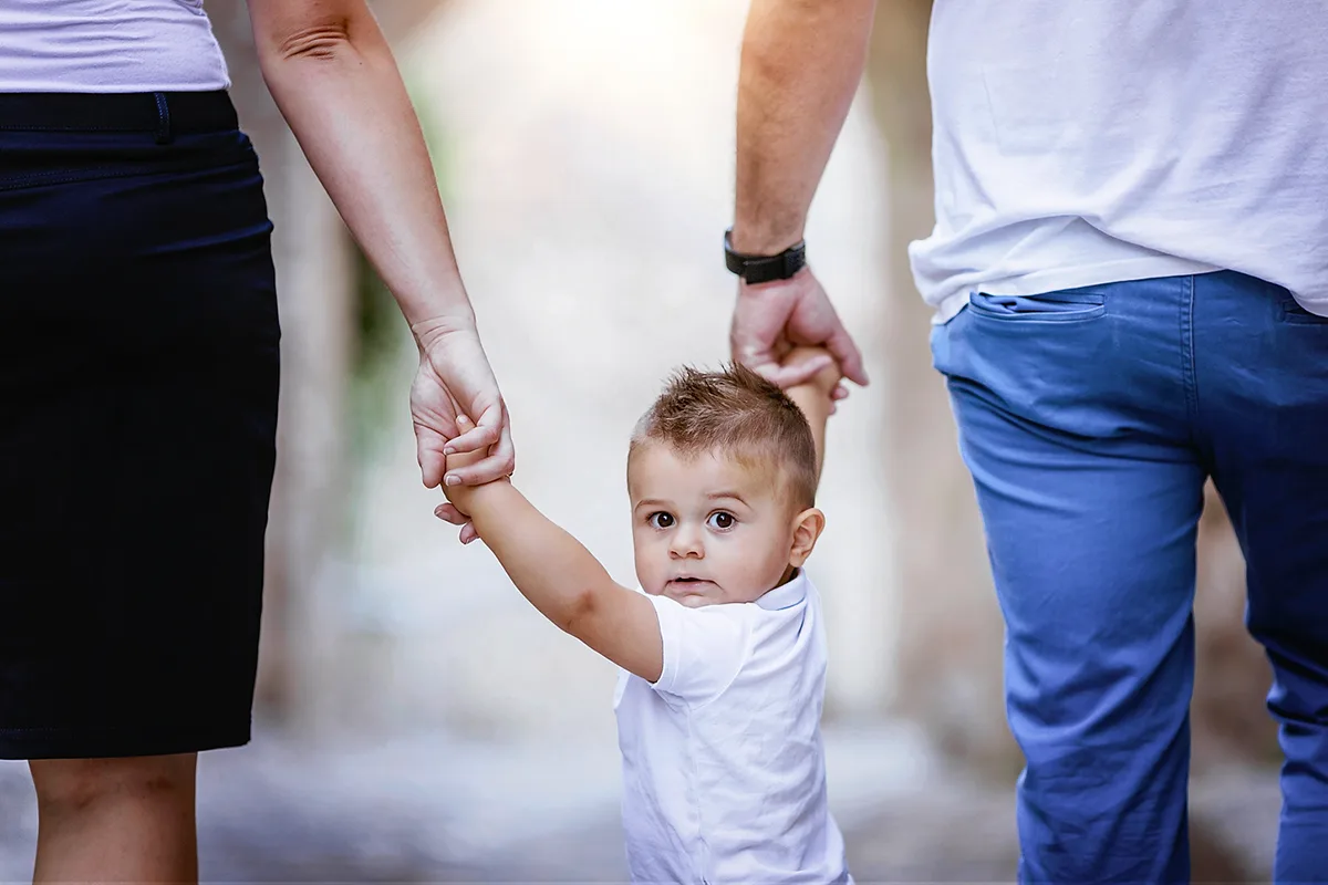 Petit garçon tenant les mains de ses parents lors d’une séance photo famille en extérieur.