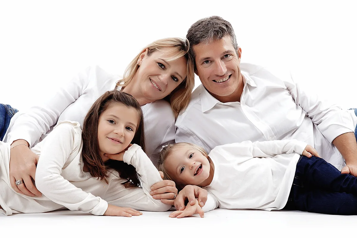 Parents avec leurs deux filles réunis lors d’une séance photo de famille sur fond blanc en studio.