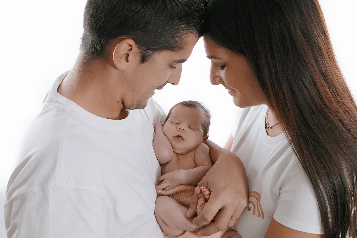 Jeunes parents contemplant leur nouveau-né endormi lors d’une séance photo naissance en famille au studio.