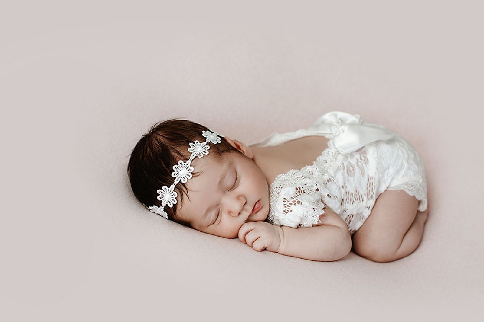 Nouveau-né endormi en tenue blanche en dentelle lors d’une séance photo naissance en studio.