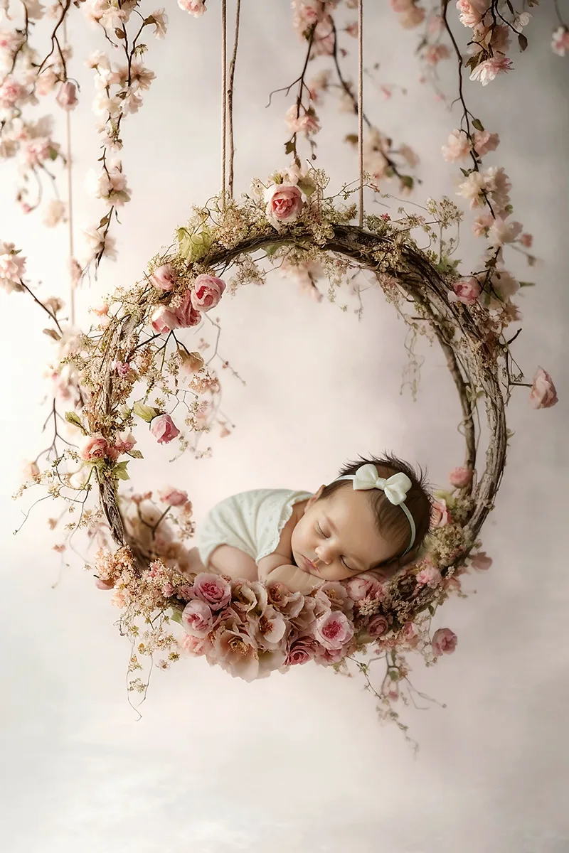 Nouveau-né endormi dans une balançoire ronde décorée de fleurs roses lors d’une séance naissance en studio dans le Luberon.